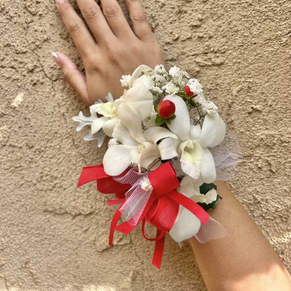 White floral wrist corsage with red ribbon on a hand