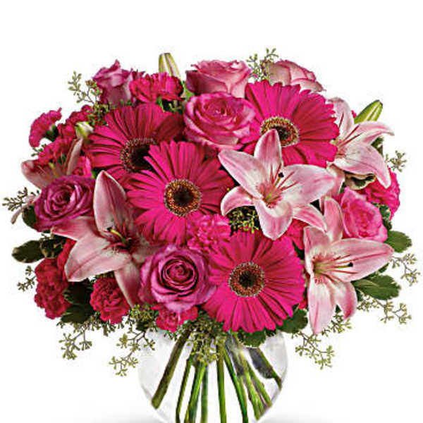 Pink gerbera daisies, roses, and lilies in a clear glass vase