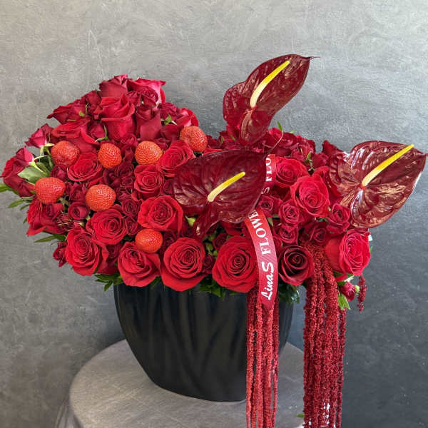 Red rose arrangement in a black vase with anthuriums and hanging red accents
