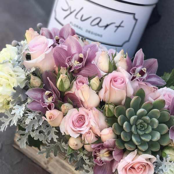 Pink roses and purple orchids arranged with succulents in a wooden box