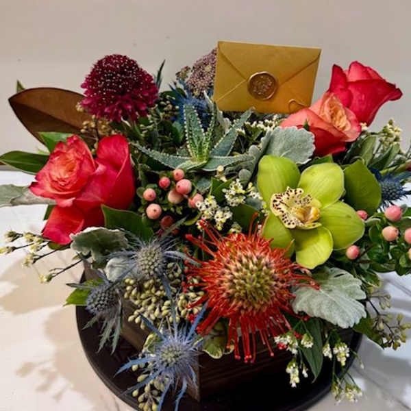 Mixed bouquet with roses, orchids, and thistle in a dark container