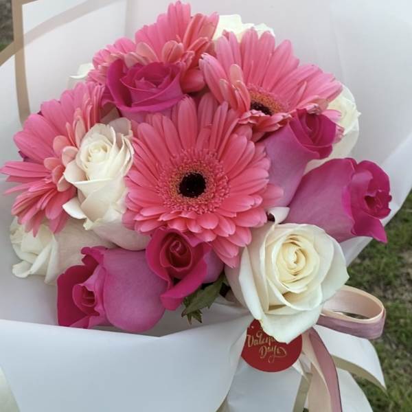 Pink gerbera daisies and roses wrapped in white paper