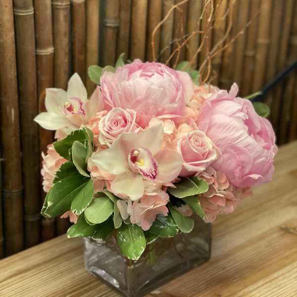 Pink floral arrangement in a square glass vase with roses and orchids