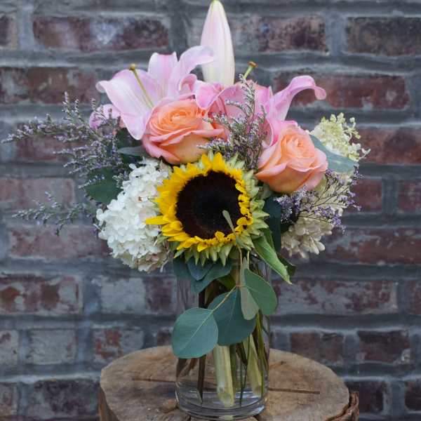 Bouquet of pink lilies, peach roses, and a sunflower in a glass vase