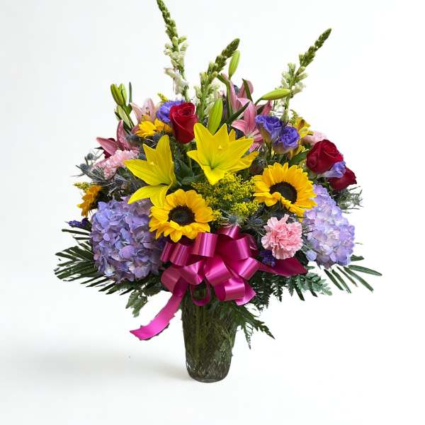 Mixed bouquet of lilies, roses, sunflowers, and hydrangeas in a glass vase