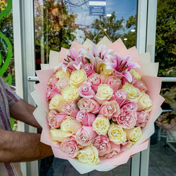 Bouquet of pink and cream roses with lilies wrapped in pastel paper