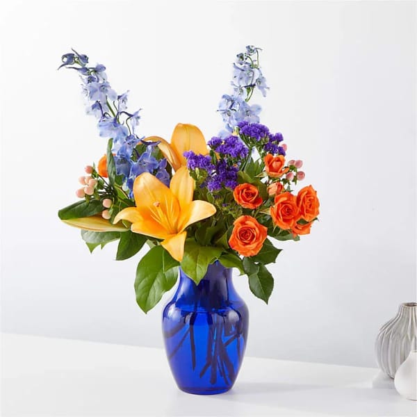 Bouquet of orange roses and yellow lilies in a blue glass vase