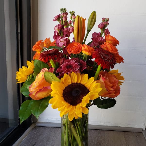 Mixed bouquet of sunflowers, roses, and orange blooms in a glass vase