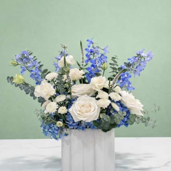 Blue and white floral arrangement in a white container