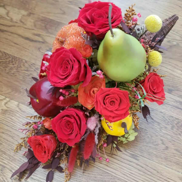 Red roses arranged with decorative fruit accents on a wooden surface