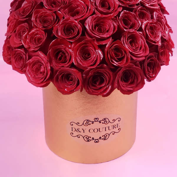 Red roses arranged in a gold round box with one gold rose