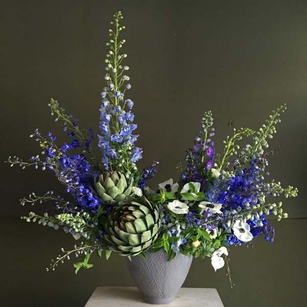 Blue and white floral arrangement with artichokes in a gray vase