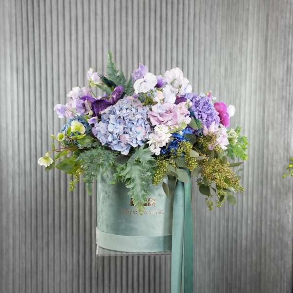 Lavender and blue floral arrangement in a mint green box with ribbon