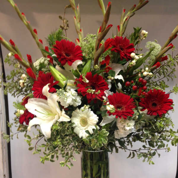Red gerbera daisies and white lilies in a tall glass vase