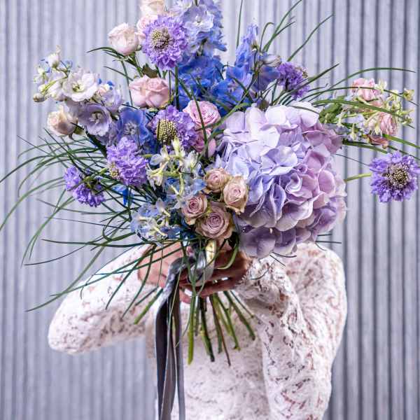 Bride holding a large pastel bouquet of hydrangeas, roses, and blue flowers