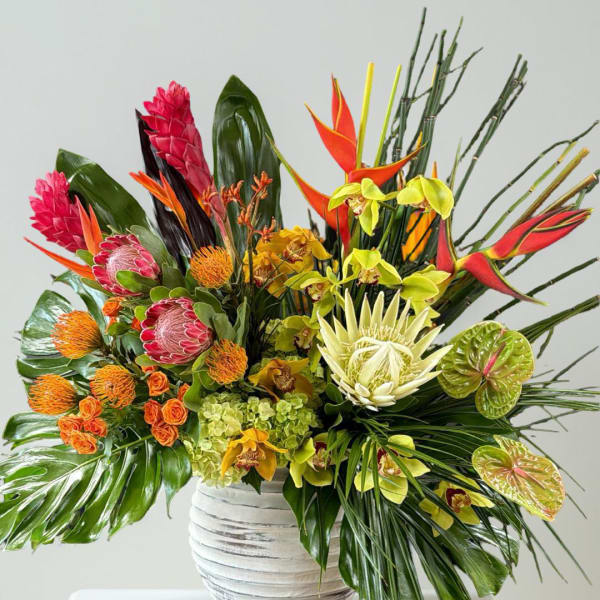 Tropical flower arrangement in a white vase with bright red, orange, yellow, and green blooms
