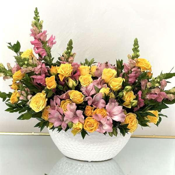 Yellow roses and pink snapdragons arranged in a white bowl vase