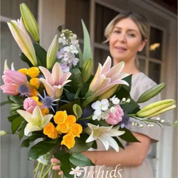 Large bouquet of lilies, roses, and small white flowers in a glass vase