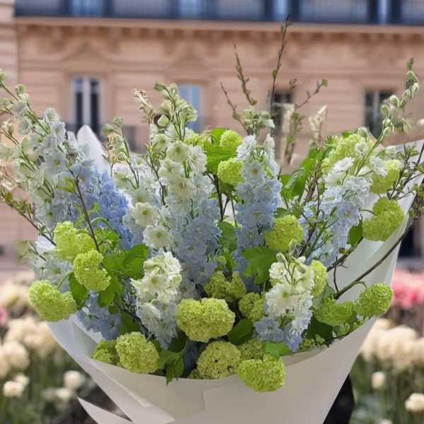 Bouquet of pale blue and white flowers with lime-green blooms wrapped in white paper