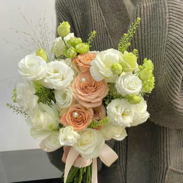 Bouquet of white and peach roses with pale green accents and ribbon