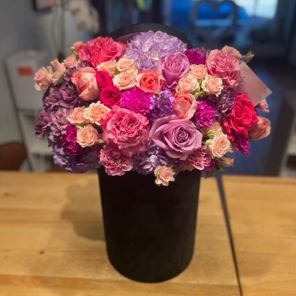 Bouquet of pink, purple, and peach roses in a black vase