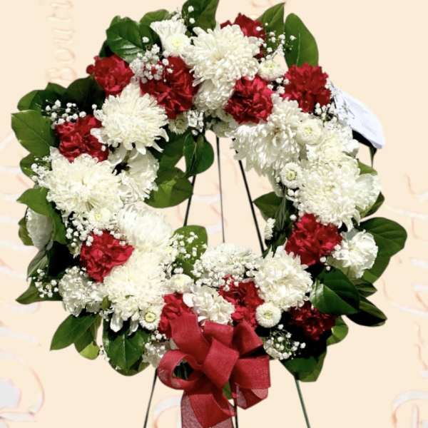 Red and white floral wreath with a red ribbon bow on a stand