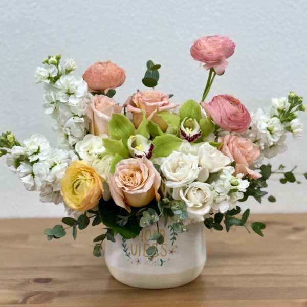 Mixed bouquet of pastel roses, ranunculus, and white blooms in a ceramic vase