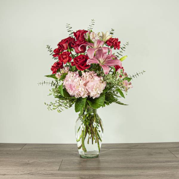 Bouquet of red roses, pink lilies, and pale hydrangea in a clear glass vase