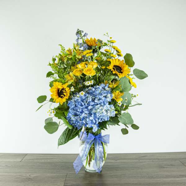 Bouquet of sunflowers, blue hydrangea, and yellow blooms in a glass vase