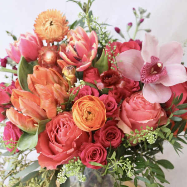 Mixed bouquet of pink, orange, and red flowers in a glass vase
