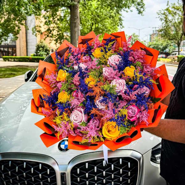 Large bouquet of multicolored roses wrapped in bright orange paper