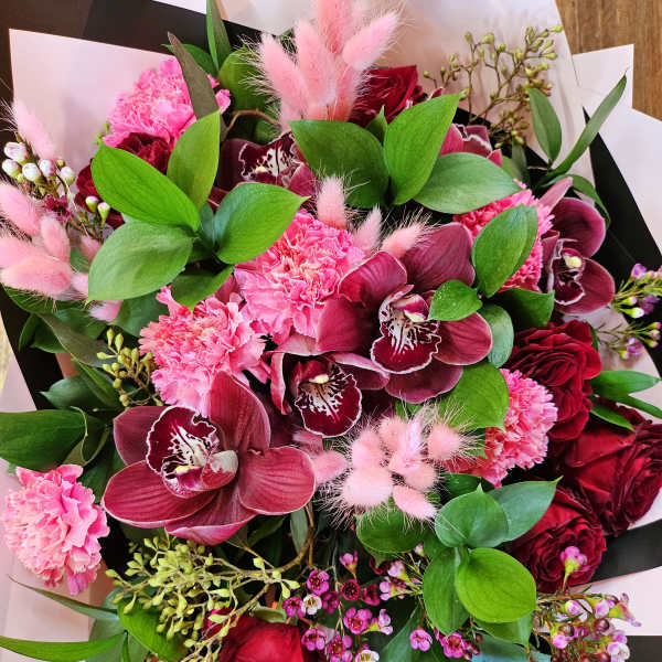Bouquet of pink and burgundy flowers with green foliage and black-and-white wrap