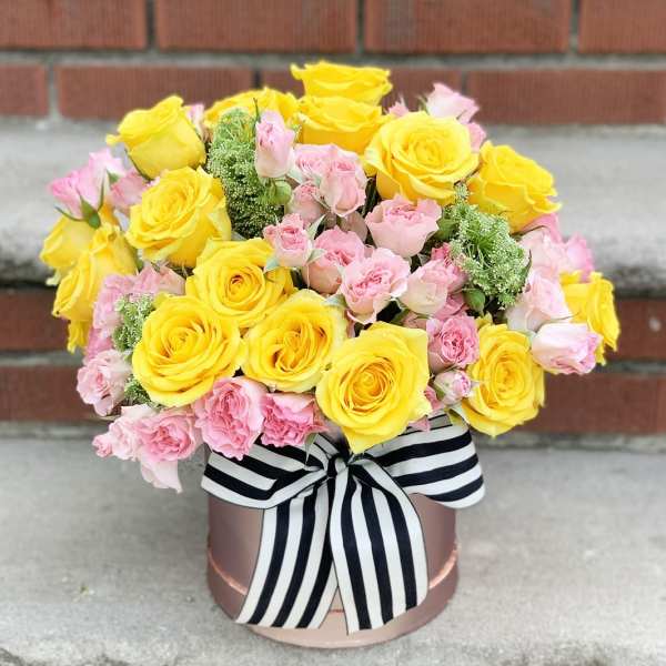 Yellow and pink rose bouquet in a round box with a striped ribbon