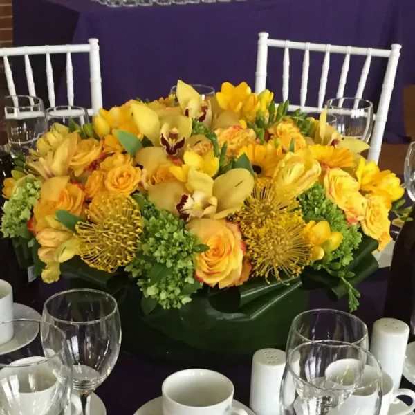 Yellow floral centerpiece in a low green container on a table