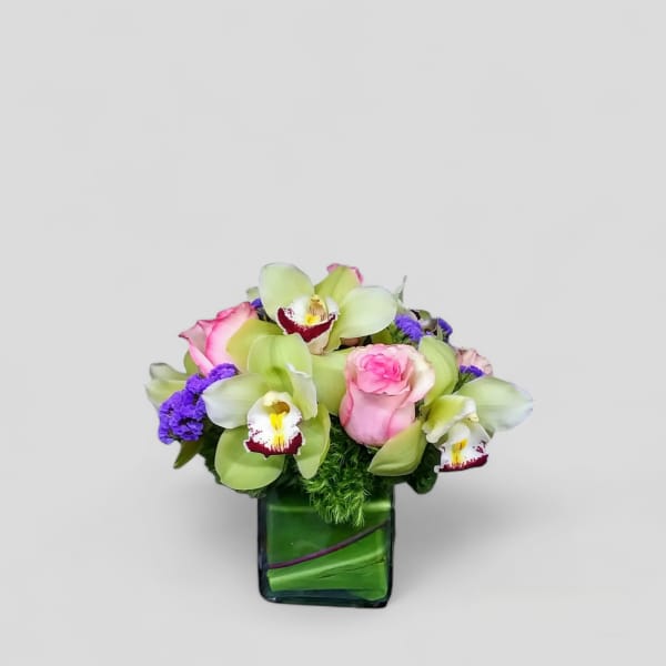 Pink roses and green orchids in a square glass vase