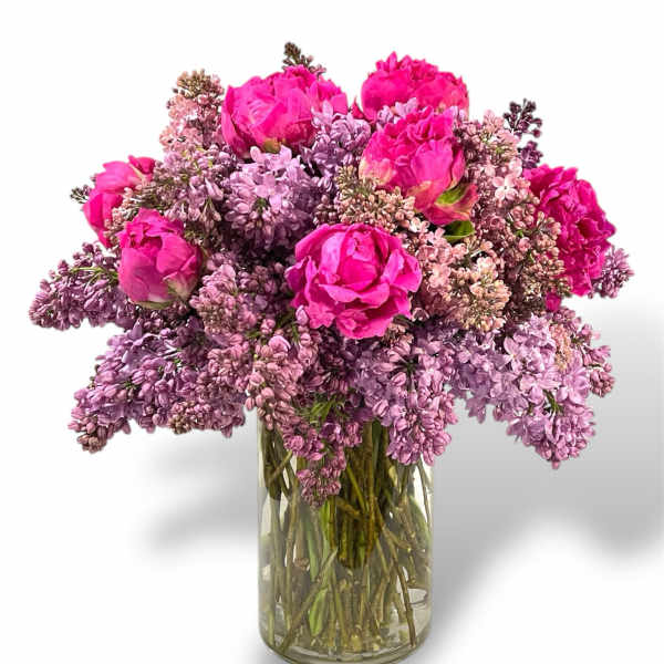 Pink peonies and lilac blooms arranged in a clear glass vase