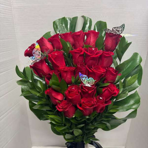 Bouquet of red roses in a tall vase with green leaves and butterfly picks