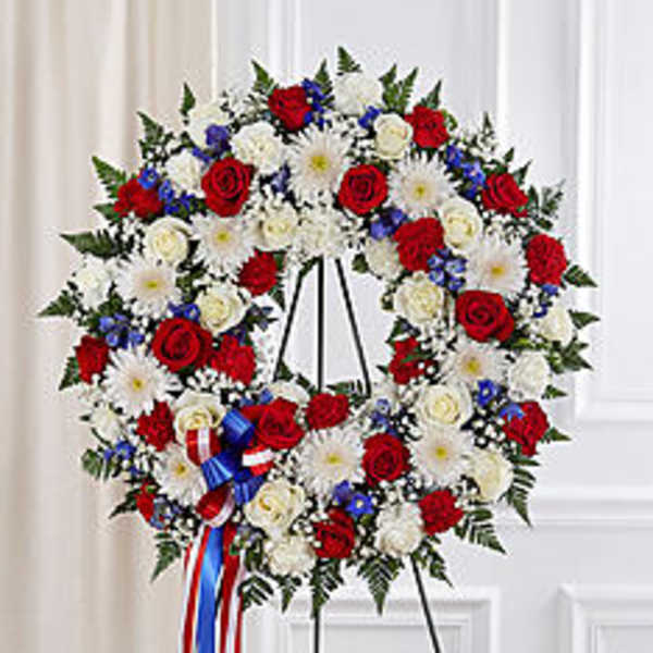 Red, white, and blue floral wreath on a stand with ribbon streamers