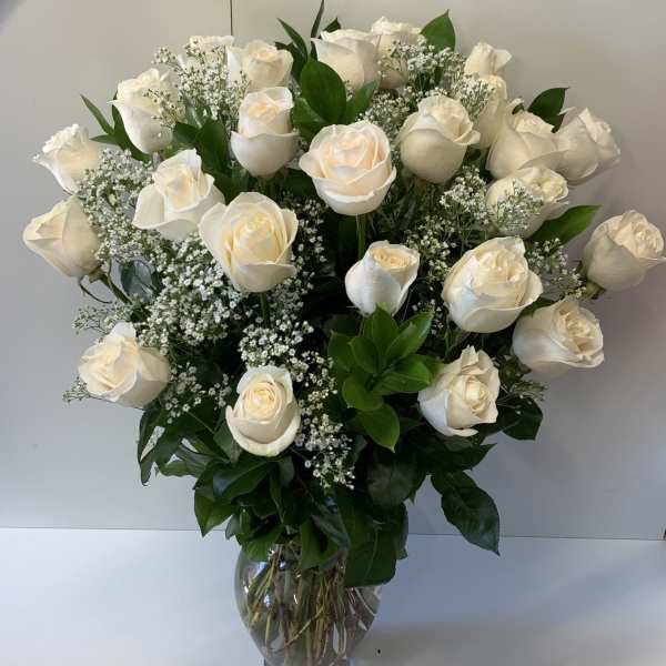 Tall arrangement of ivory roses with white filler flowers in a clear glass vase