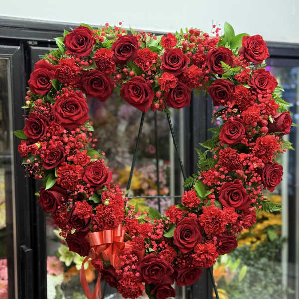 Heart-shaped red rose wreath on a stand with a ribbon bow
