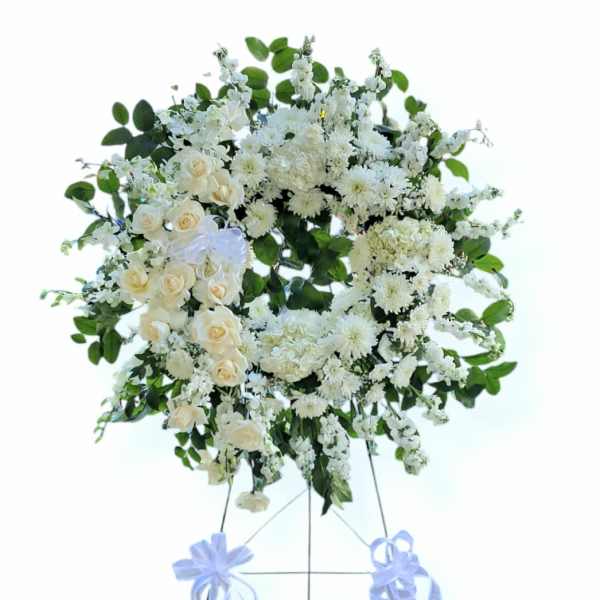 White floral standing wreath on an easel with blue ribbons