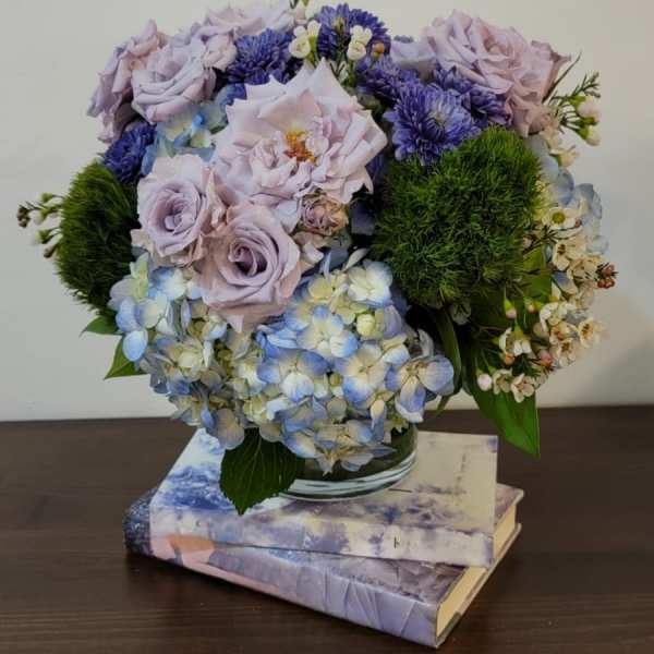 Lavender roses and blue hydrangeas arranged in a glass vase