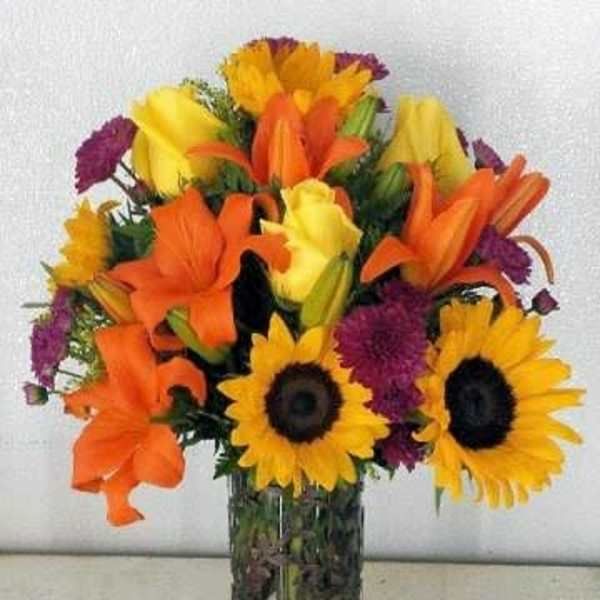 Bouquet of sunflowers, orange lilies, and purple flowers in a glass vase