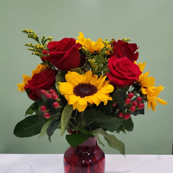 Bouquet of red roses and yellow sunflowers in a red glass vase