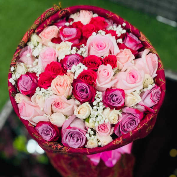 Round bouquet of pink, red, and lavender roses with white filler flowers