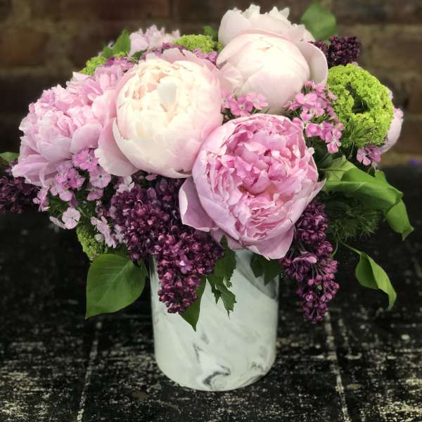 Pink peonies and purple blooms arranged in a white vase