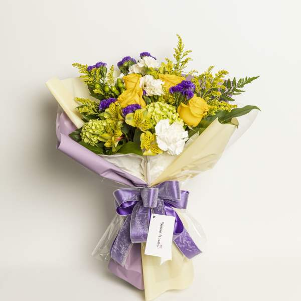 Bouquet of yellow roses, white flowers, and purple accents wrapped in lavender and cream paper