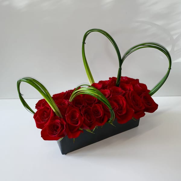 Red roses in a black rectangular container with green looped accents
