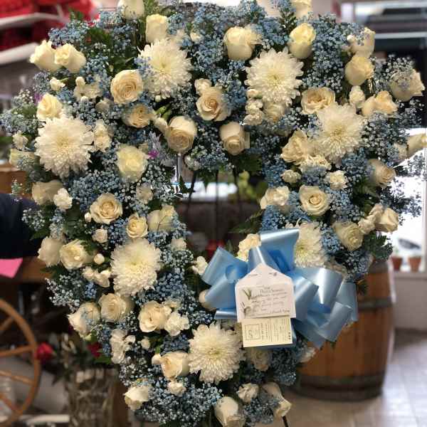 Heart-shaped floral wreath of white roses and blue filler flowers with a blue bow