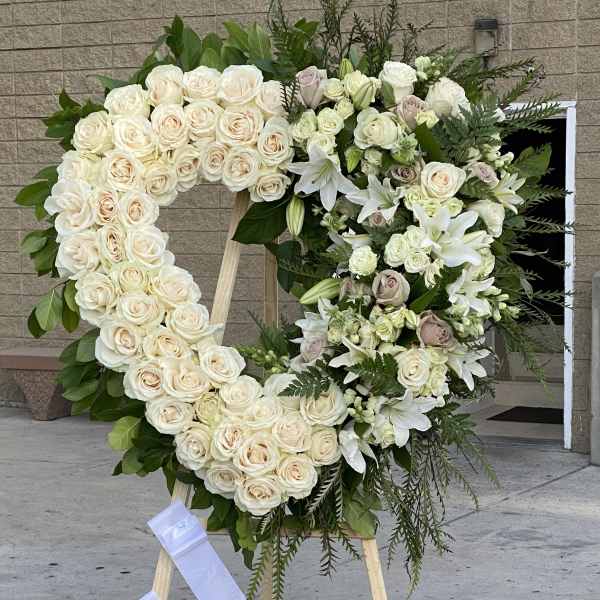 Heart-shaped floral wreath of white roses and lilies on an easel